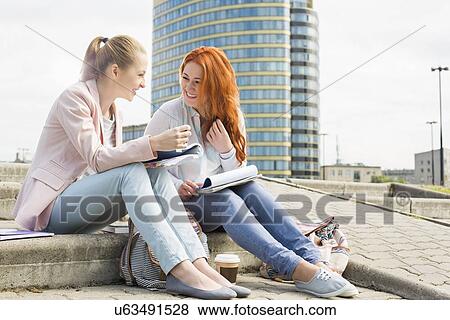 Full length of smiling female college students studying on steps against building View Large Photo Image Stock Photo - Full length of smiling female college students studying on steps against building. Fotosearch