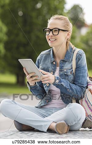 Full length of smiling young female college student using tablet PC in park View Large Photo Image Stock Photo - Full length of smiling young female college student using tablet PC in park. Fotosearch