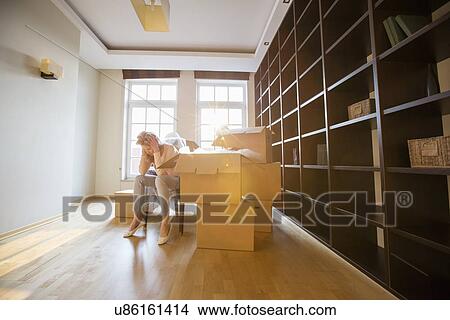 Picture - Full-length of stressed woman sitting by cardboard boxes in new house. Fotosearch