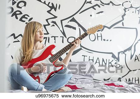 Stock Photography - Full-length of teenage girl playing guitar in bedroom. Fotosearch