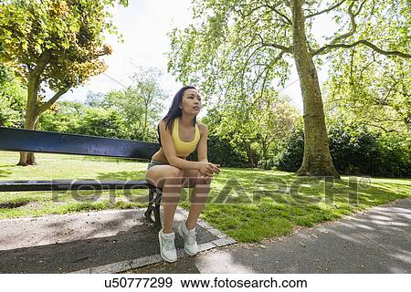 Stock Photo - Full length of tired fit woman sitting on beach while exercising in park. Fotosearch