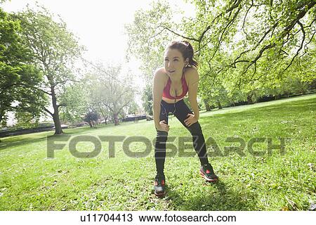 Stock Image - Full length of tired fit woman taking break while exercising in park. Fotosearch