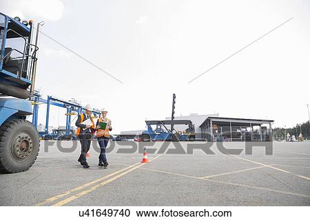 Stock Image - Full-length of workers walking in shipping yard. Fotosearch