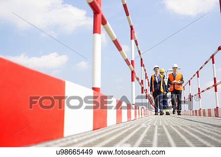 Full-length of workers walking on footbridge against sky View Large Photo Image Stock Photo - Full-length of workers walking on footbridge against sky. Fotosearch
