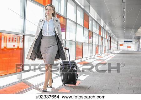Picture - Full length of young businesswoman with luggage walking in railroad station. Fotosearch