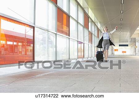 Stock Image - Full length of young businesswoman with luggage rushing in railroad station. Fotosearch