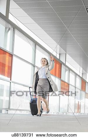 Stock Image - Full length of young businesswoman with luggage rushing in railroad station. Fotosearch