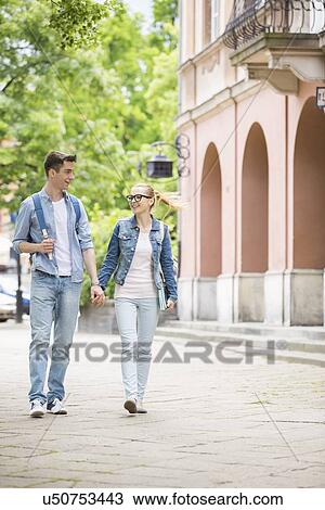 Stock Image - Full length of young college couple talking while walking in campus. Fotosearch