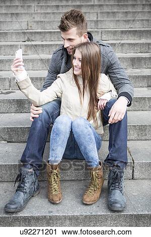 Full length of young couple taking picture of themselves while sitting on steps outdoors View Large Photo Image Stock Image - Full length of young couple taking picture of themselves while sitting on steps outdoors. Fotosearch