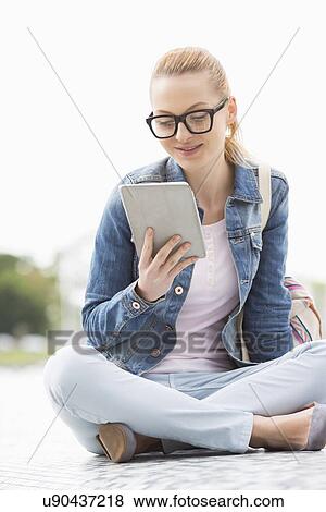 Stock Photo - Full length of young female college student using tablet PC in park. Fotosearch