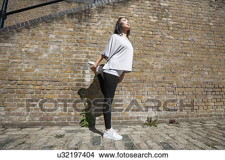 Picture - Full length of young fit woman stretching against brick wall. Fotosearch
