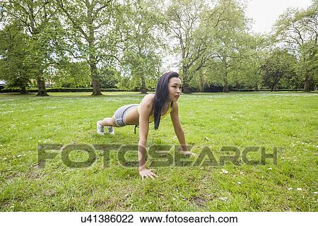 Stock Image - Full length of young fit woman performing pushups at park. Fotosearch