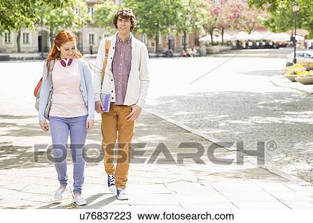 Stock Image - Full length of young male and female college students walking on footpath. Fotosearch