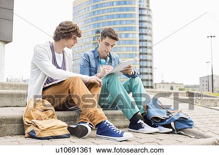 Stock Image - Full length of young male college students studying on steps against building. Fotosearch