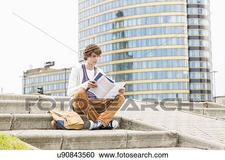 Full length of young male college student reading book against building View Large Photo Image Stock Image - Full length of young male college student reading book against building. Fotosearch
