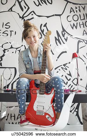 Full-length portrait of girl with electric guitar sitting on study table at home View Large Photo Image Stock Photograph - Full-length portrait of girl with electric guitar sitting on study table at home. Fotosearch