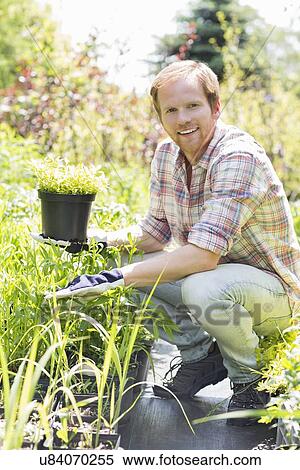 Stock Photography - Full-length portrait of happy man holding potted plant at garden. Fotosearch
