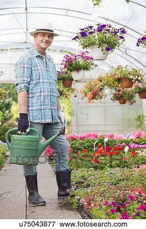 Full-length portrait of smiling man carrying watering can in greenhouse View Large Photo Image Stock Photo - Full-length portrait of smiling man carrying watering can in greenhouse. Fotosearch