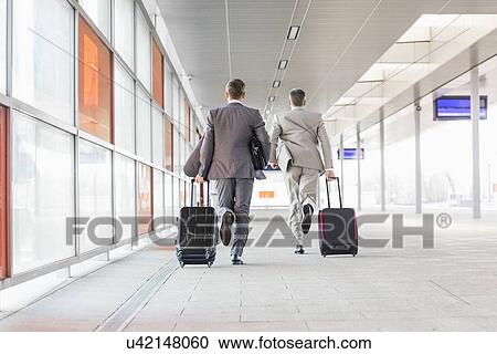 Stock Image - Full length rear view of businessmen with luggage running on railroad platform. Fotosearch