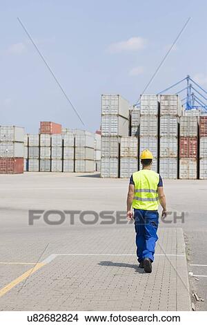 Full-length rear view of male worker walking in shipping yard View Large Photo Image Picture - Full-length rear view of male worker walking in shipping yard. Fotosearch