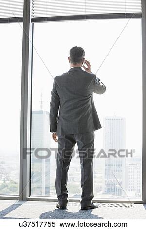 Full length rear view of mature businessman using cell phone white standing near window View Large Photo Image Stock Photography - Full length rear view of mature businessman using cell phone white standing near window. Fotosearch