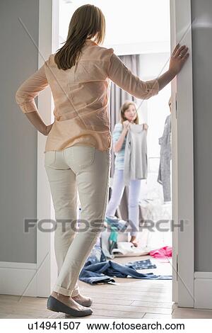 Stock Photo - Full-length rear view of mother watching daughters trying on clothes in room. Fotosearch