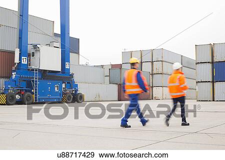 Stock Photo - Full-length rear view of workers walking in shipping yard. Fotosearch