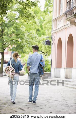 Stock Photography - Full length rear view of young college friends talking while walking in campus. Fotosearch