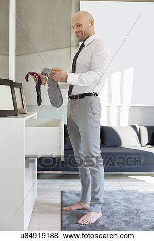 Stock Photo - Full length side view of businessman selecting socks at home. Fotosearch