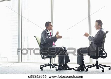 Full-length side view of businessmen discussing while sitting on office chairs by window View Large Photo Image Stock Photography - Full-length side view of businessmen discussing while sitting on office chairs by window. Fotosearch