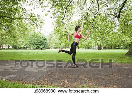 Stock Image - Full length side view of fit woman jogging in park. Fotosearch