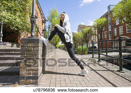 Stock Photograph - Full length side view of young fit woman stretching on sidewalk. Fotosearch