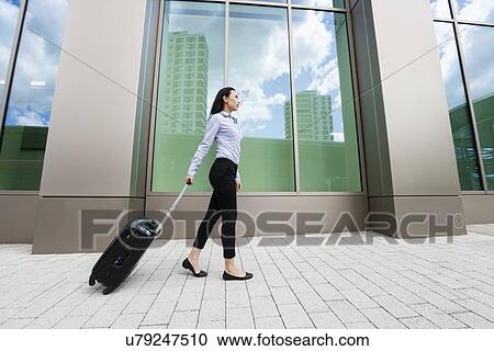 Full length side view of young businesswoman walking with luggage on sidewalk against building View Large Photo Image Stock Image - Full length side view of young businesswoman walking with luggage on sidewalk against building. Fotosearch