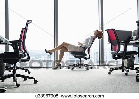 Full length side view of young businesswoman leaning back in chair at office View Large Photo Image Stock Photography - Full length side view of young businesswoman leaning back in chair at office. Fotosearch