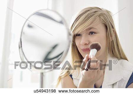 Girl applying makeup in front of mirror at home View Large Photo Image Stock Photo - Girl applying makeup in front of mirror at home. Fotosearch
