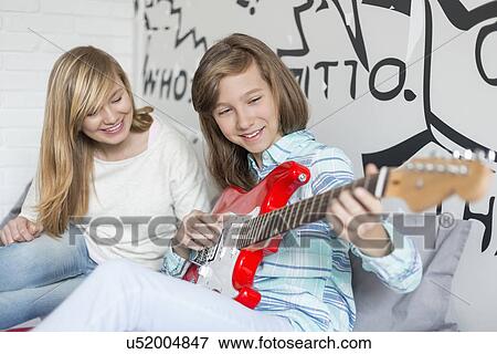 Girl listening to sister playing guitar at home View Large Photo Image Stock Photo - Girl listening to sister playing guitar at home. Fotosearch