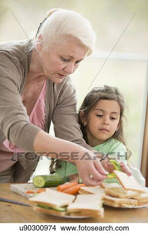 Picture - Girl looking at grandmother preparing sandwiches at home. Fotosearch