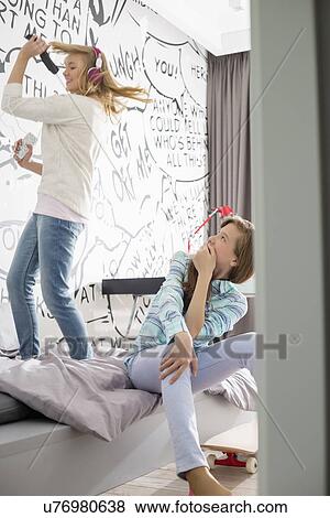 Girl watching sister singing into hairbrush in bedroom View Large Photo Image Stock Photo - Girl watching sister singing into hairbrush in bedroom. Fotosearch