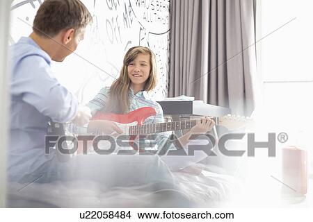 Picture - Girl with father playing electric guitars at home. Fotosearch