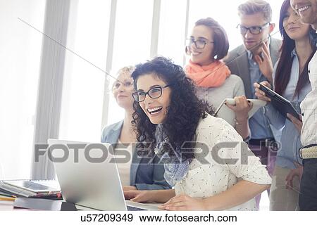 Group of cheerful businesspeople with laptop at desk in creative office View Large Photo Image Stock Photo - Group of cheerful businesspeople with laptop at desk in creative office. Fotosearch
