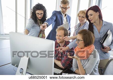 Stock Image - Group of smiling businesspeople using computer together in office. Fotosearch