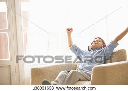 Happy boy with arms raised enjoying music while relaxing on armchair at home View Large Photo Image Stock Image - Happy boy with arms raised enjoying music while relaxing on armchair at home. Fotosearch