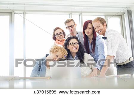 Stock Photography - Happy business colleagues with laptop discussing in creative office. Fotosearch