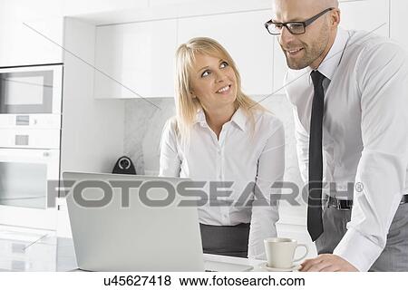 Happy business couple working on laptop in kitchen View Large Photo Image Stock Photo - Happy business couple working on laptop in kitchen. Fotosearch