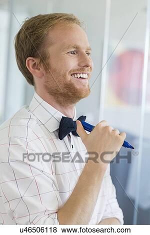 Happy businessman looking away while holding felt tip pen at creative office View Large Photo Image Stock Photo - Happy businessman looking away while holding felt tip pen at creative office. Fotosearch