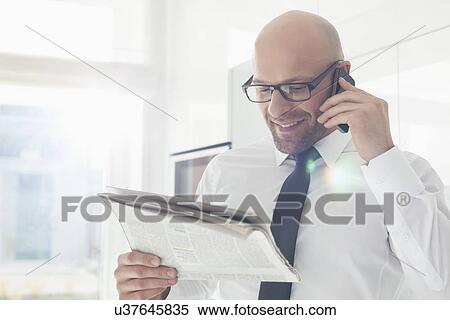 Stock Photography - Happy businessman on call while reading newspaper at home. Fotosearch