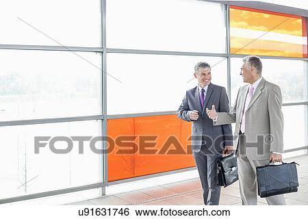 Stock Photograph - Happy businessmen talking while walking in railroad station. Fotosearch