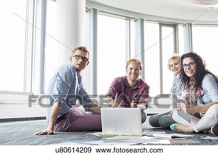 Happy businesspeople looking away while working on floor at creative office View Large Photo Image Stock Photo - Happy businesspeople looking away while working on floor at creative office. Fotosearch