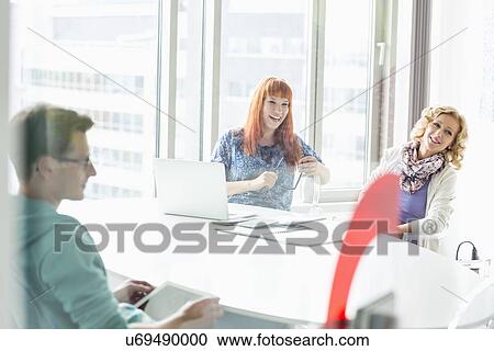 Happy businesspeople sitting at desk in creative office View Large Photo Image Stock Image - Happy businesspeople sitting at desk in creative office. Fotosearch