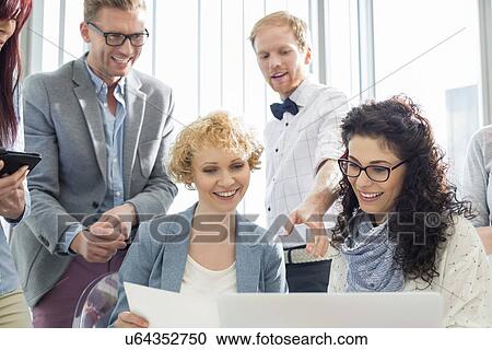 Happy businesspeople working on laptop in creative office View Large Photo Image Stock Image - Happy businesspeople working on laptop in creative office. Fotosearch